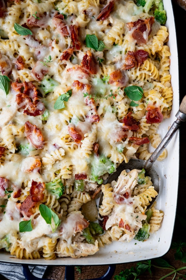 Close up overhead shot of an easy chicken bacon ranch casserole in a dish with a serving spoon and fresh herbs garnish