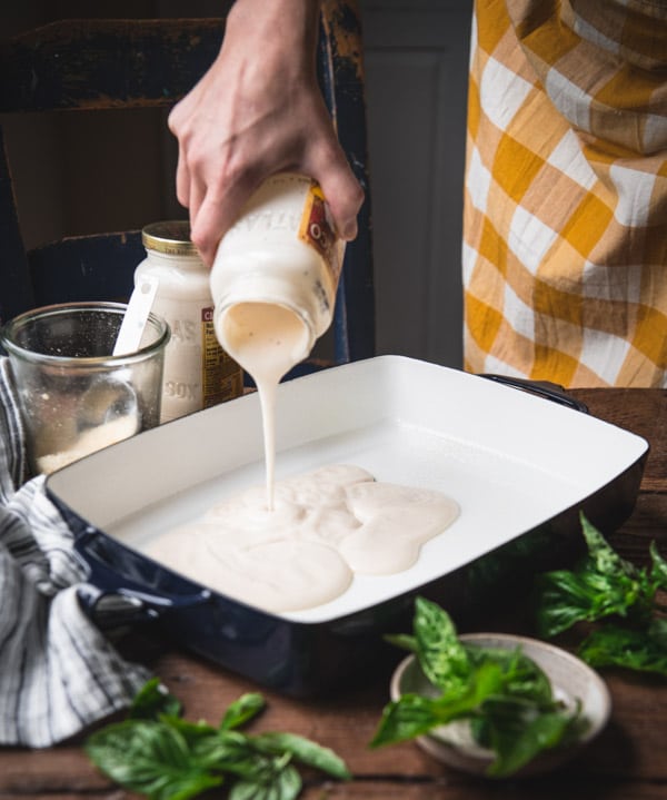 Pouring Alfredo sauce into a baking dish