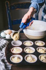 Scooping muffin batter into muffin tins.