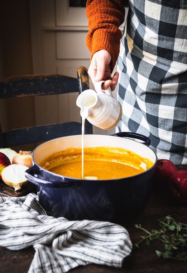 Pouring cream into a pot of pumpkin soup