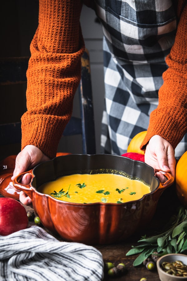Hands holding a cast iron Dutch oven full of creamy pumpkin soup