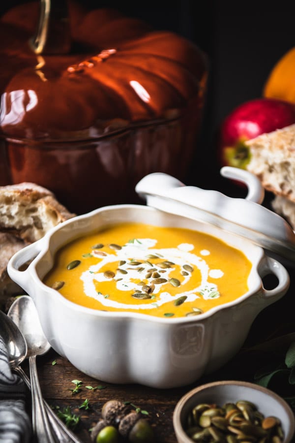 Side shot of a bowl of creamy pumpkin soup served with a side of bread