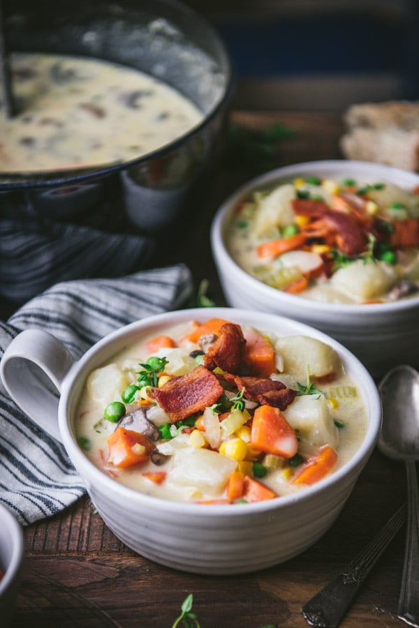 Side shot of two bowls of creamy vegetable chowder on a wooden table