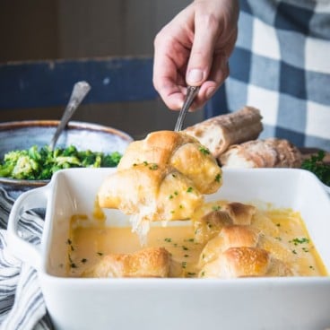 Hands serving crescent roll chicken casserole with broccoli and cheese sauce