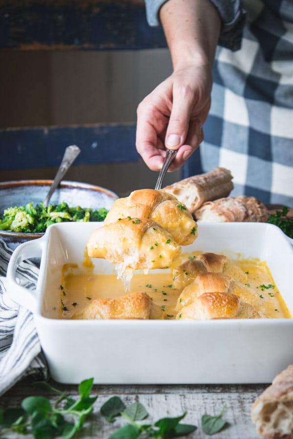 Hands serving crescent roll chicken casserole with broccoli and cheese sauce
