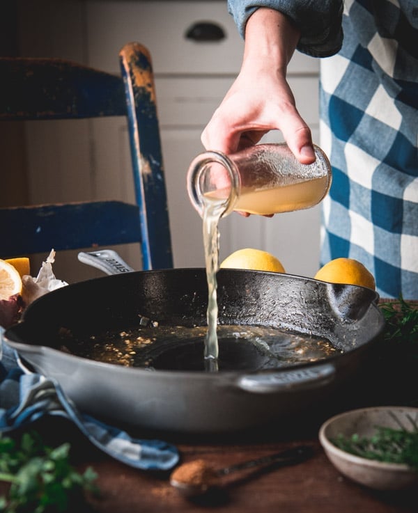 Pouring broth into a cast iron skillet.