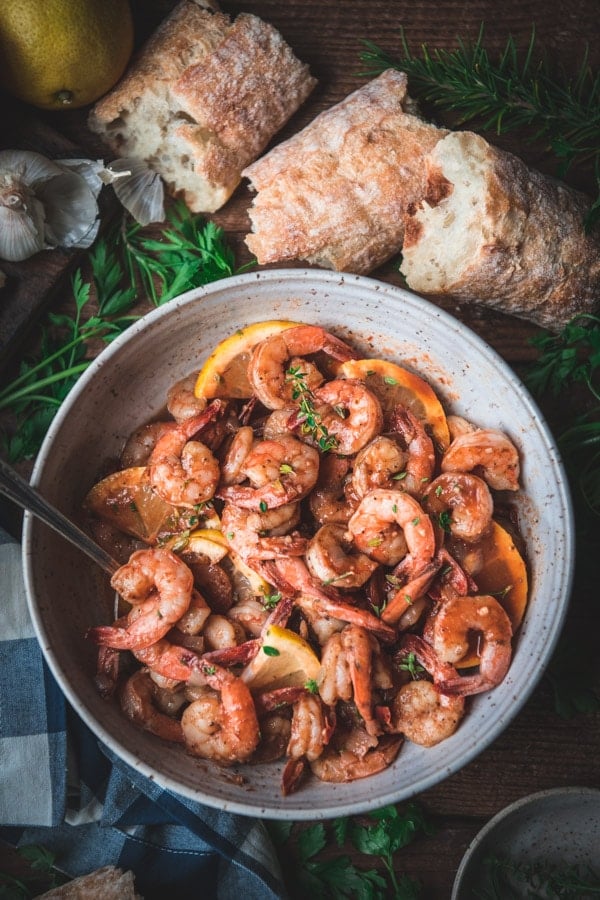 Overhead shot of a bowl of garlic butter shrimp recipe on a table with a loaf of crusty French baguette.