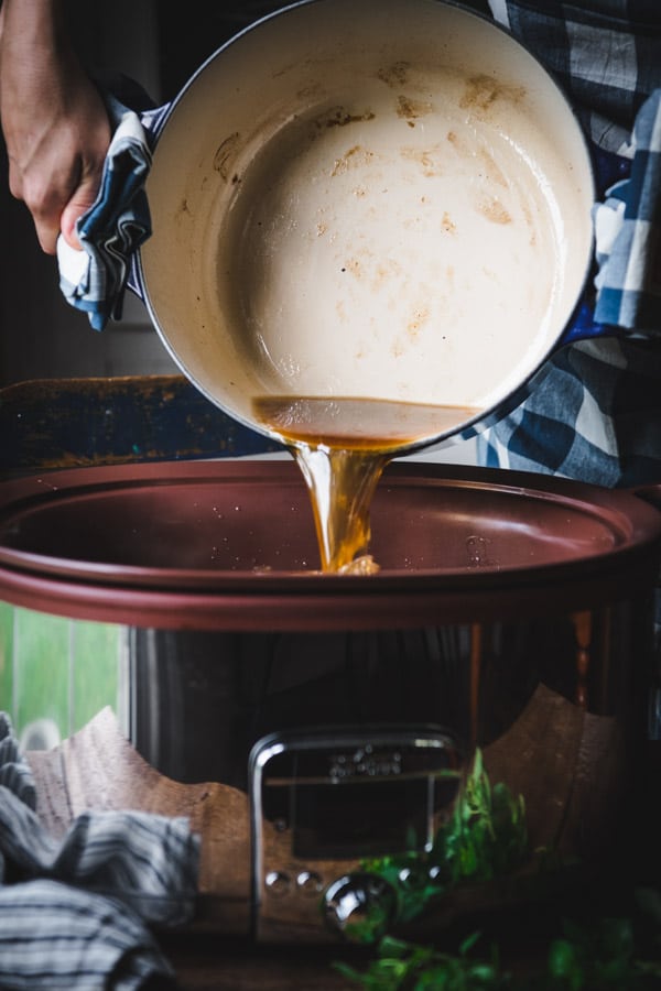 Pouring beef broth from a Dutch oven into a Crock Pot