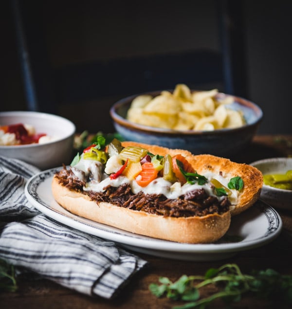 Square image of slow cooker Italian beef sandwich on a dinner table