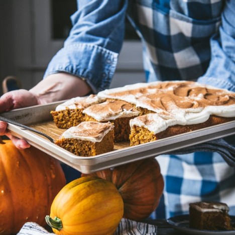 Hands holding a sheet pan of pumpkin bars with cream cheese frosting.
