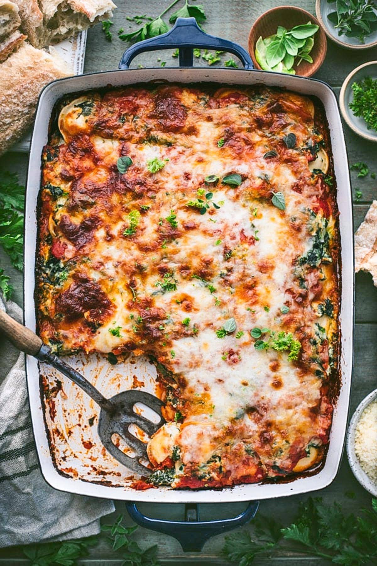 Serving spoon in a dish of baked ravioli with ricotta and spinach.