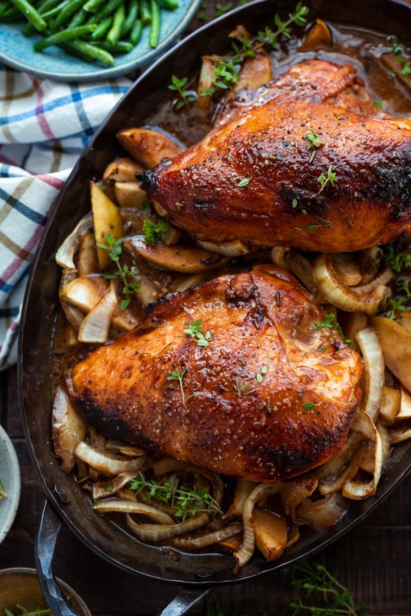 Two roasted chicken breasts sit on a bed of molasses and apple cider roasted apples and onions. The skin of the chicken breast is a perfect crispy golden-brown.