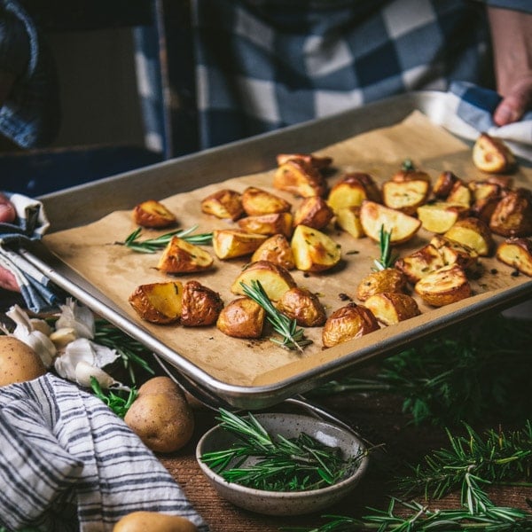 Hands holding a sheet pan of garlic rosemary roasted potatoes