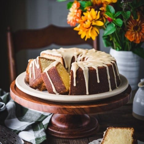 Vanilla pound cake with caramel icing on a wooden cake stand with flowers in the background