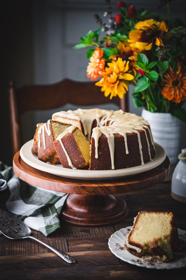 Vanilla pound cake with caramel icing on a wooden cake stand with flowers in the background