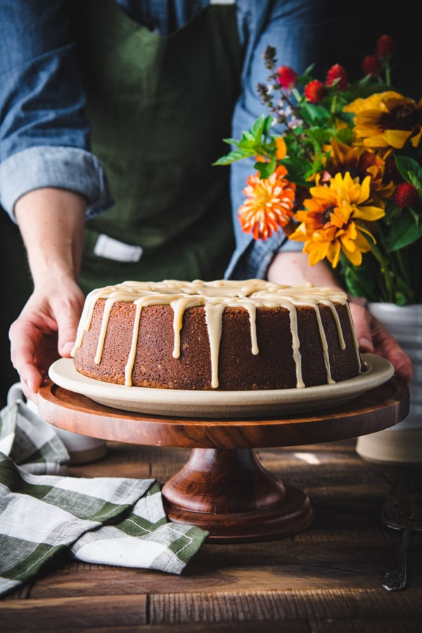 Hands holding a plate of a moist pound cake recipe on a wooden cake stand