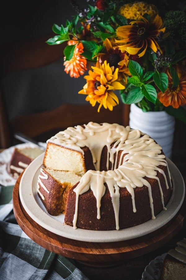 Overhead image of a sliced butter pound cake with caramel frosting on a ceramic serving platter with flowers in the background