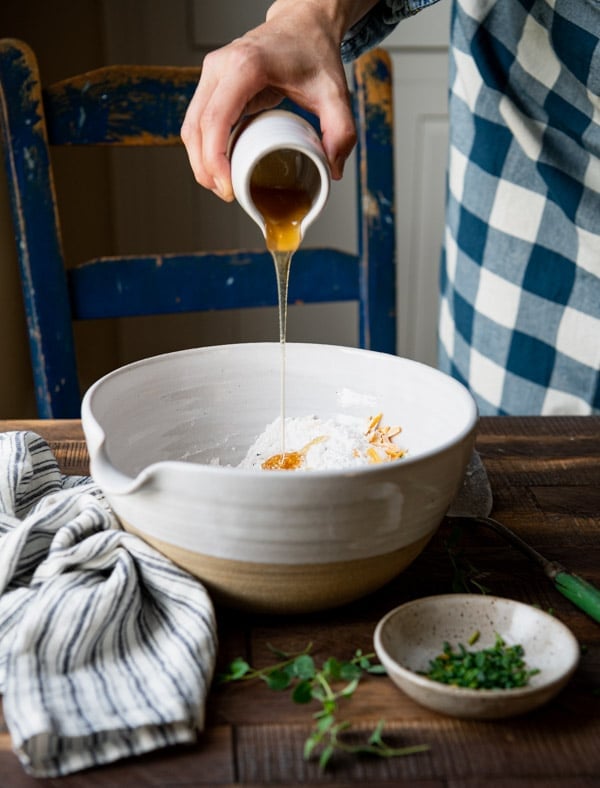 Adding honey to a large white mixing bowl