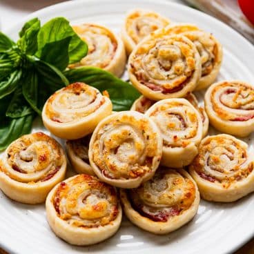 Square side shot of easy Italian appetizers on a white serving tray with fresh basil.