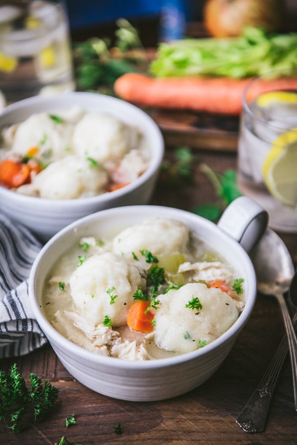 A simple chicken and dumping soup recipe served in white bowls with parsley garnish