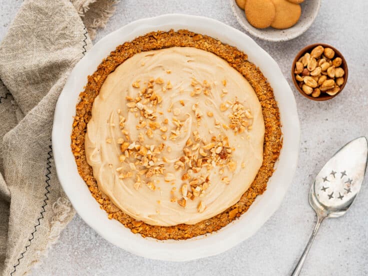 Horizontal overhead shot of a finished peanut butter pie on a white table.