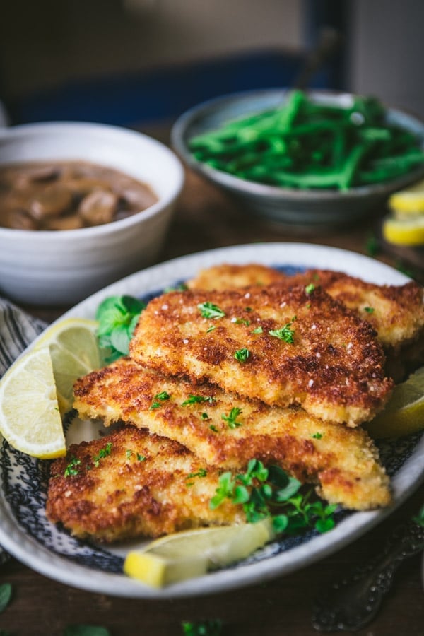 Side shot of a tray of pork schnitzel garnished with parsley and lemon wedges