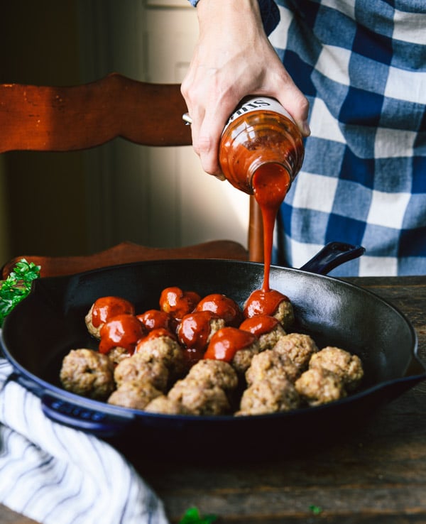 Pouring barbecue sauce over meatballs in a skillet