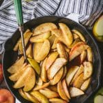 Overhead shot of baked apple slices in a skillet on a wooden farmhouse table