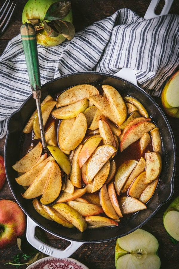 Overhead shot of baked apple slices in a skillet on a wooden farmhouse table