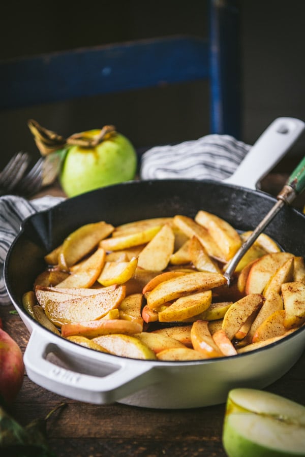 Pan of quick baked apple slices on a wooden table with fresh fruit nearby