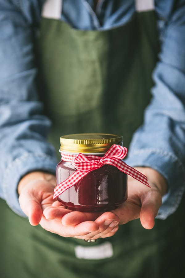 Hands holding a jar of Christmas jam with a ribbon around it for a gift