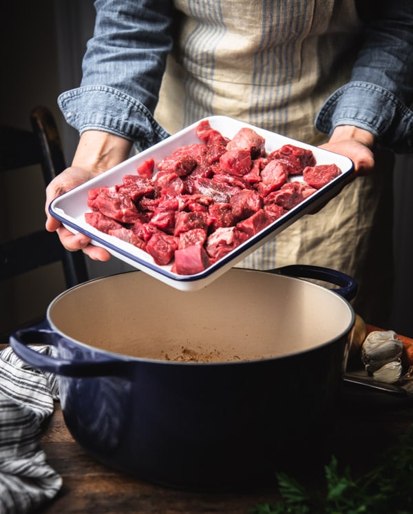 Pan of cubed beef stew meat on a tray over a Dutch oven