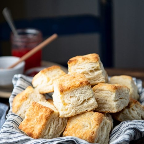 Side shot of a basket of flaky biscuits on a wooden table
