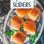 Overhead shot of baked ham and cheese sliders on a blue and white tray with text title overlay