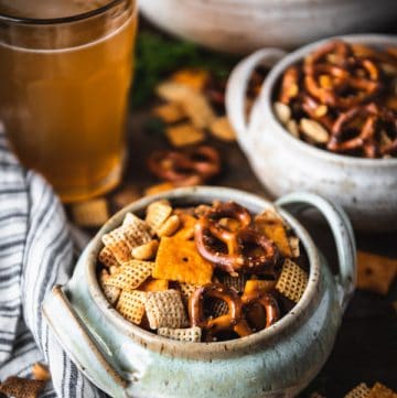 Side shot of two bowls of homemade Chex mix on a table with cold drinks