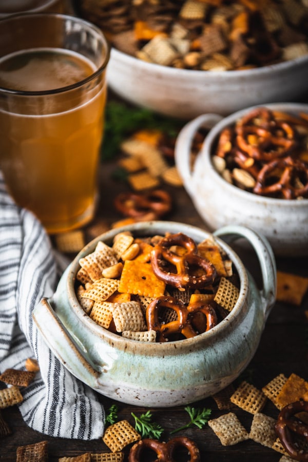 Side shot of two bowls of homemade Chex mix on a table with cold drinks