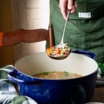 Ladle serving leftover turkey soup with wild rice from a blue dutch oven