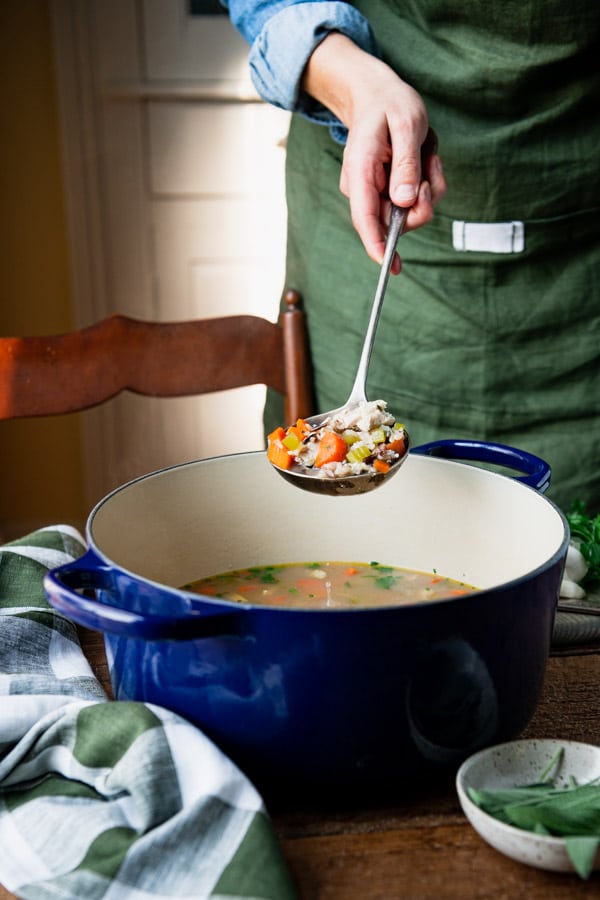 Ladle serving leftover turkey soup with wild rice from a blue dutch oven