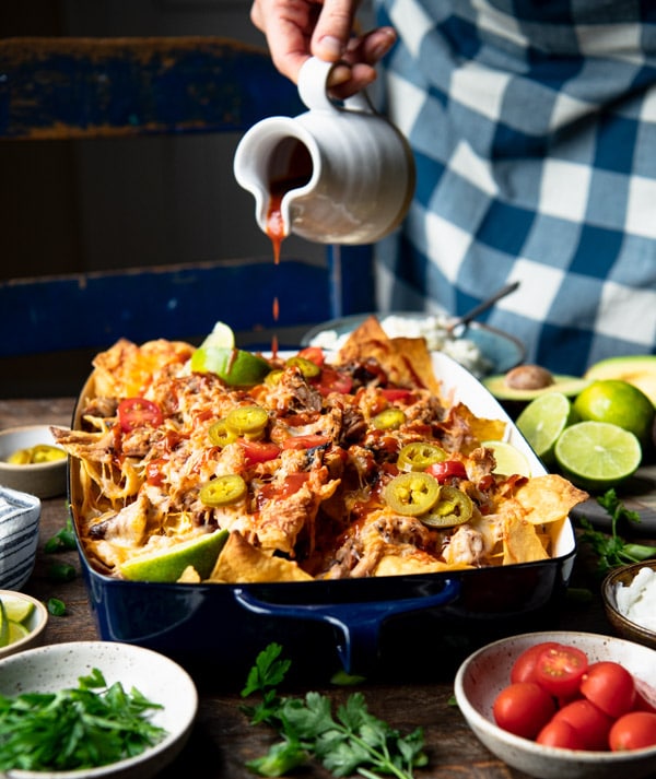 Drizzling barbecue sauce over a pan of smoked pulled pork nachos