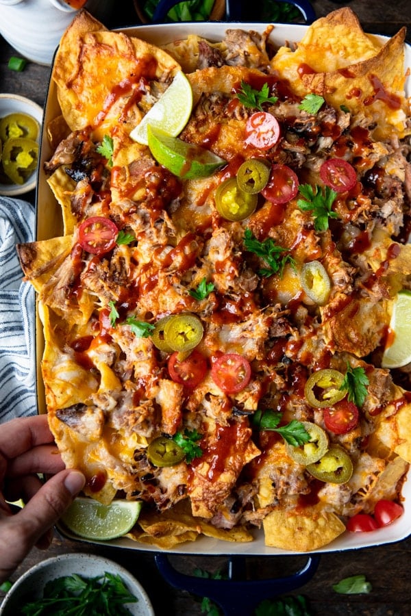 Close up shot of a hand picking up smoked pulled pork nachos from a tray