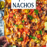 Hand picking up pulled pork nachos with text title overlay
