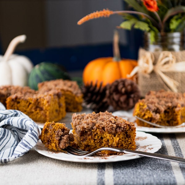 Square shot of pumpkin coffee cake on a table with pumpkins and flowers in the background