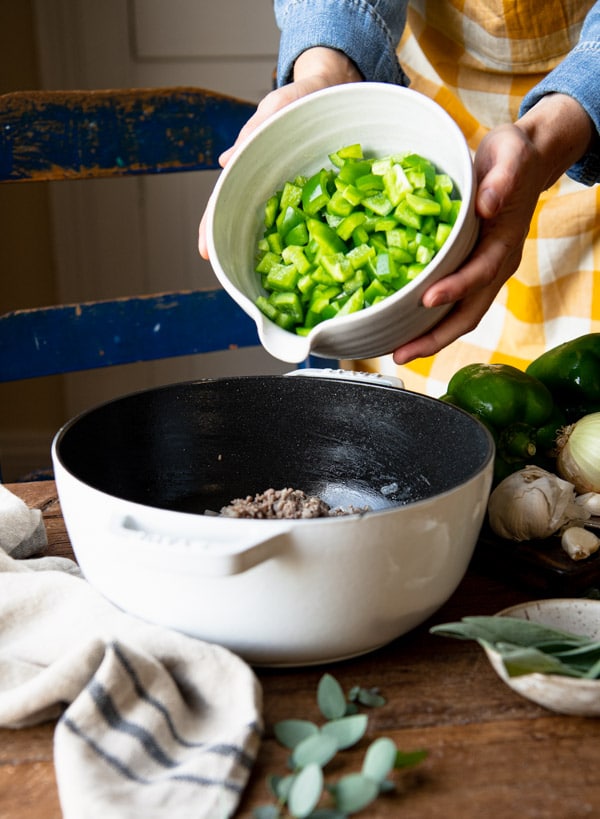Adding green bell peppers to a white Dutch oven.