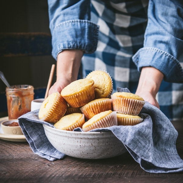 Square shot of hands serving a bowl of sweet cornbread muffins with a blue cloth