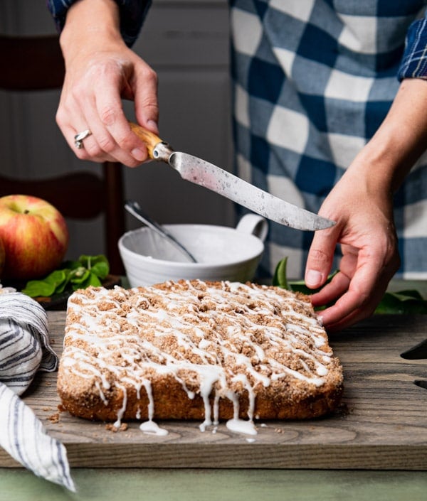 Hand holding a knife that's ready to slice a sour cream apple coffee cake