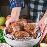 Hands serving a basket of easy apple muffins on a dinner table