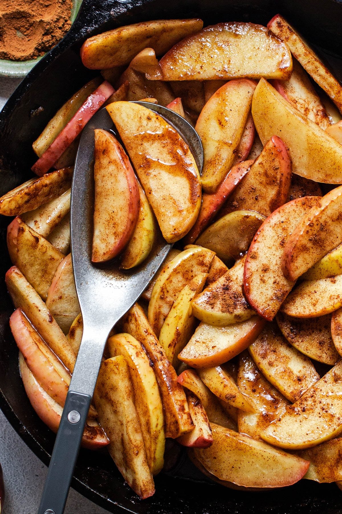 Close overhead shot of a serving spoon in a skillet of baked apple slices.