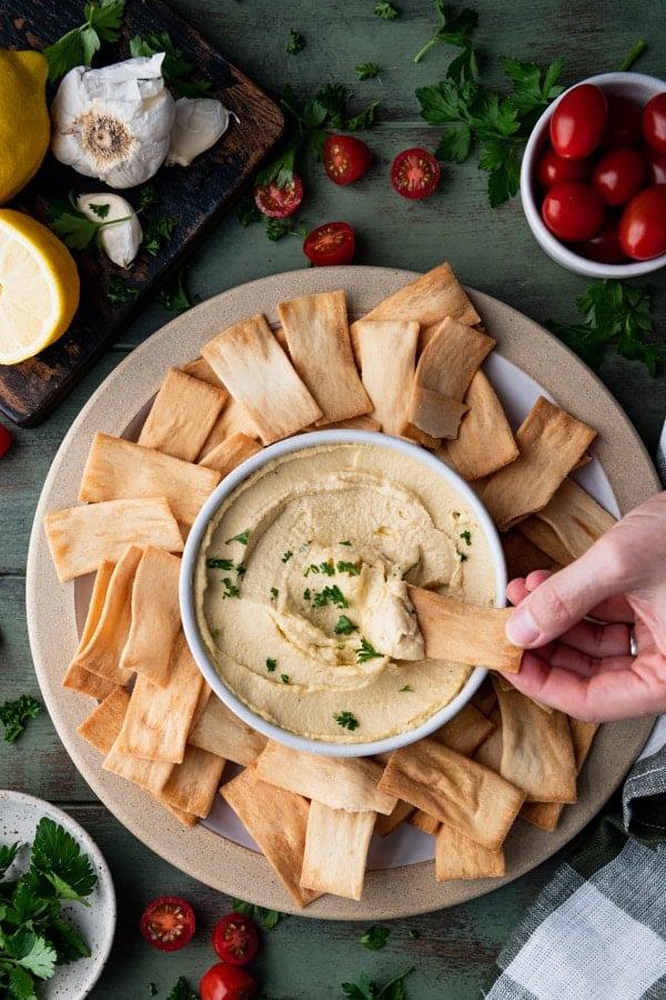 Overhead shot of hand dipping a pita chip in a bowl of homemade hummus