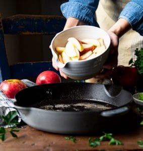 Adding a bowl of sliced apples to a cast iron skillet