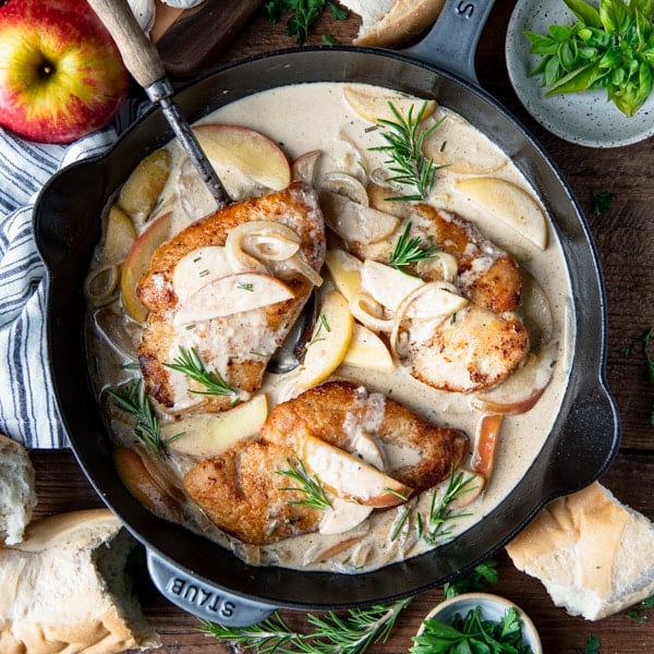 Square overhead shot of chicken with apples in a cast iron pan.